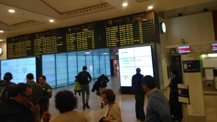 Panel de salidas de un aeropuerto con viajeros debajo