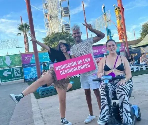Asistentes a un festival con un cartel sobre reducción de las desigualdades, una persona en silla de ruedas