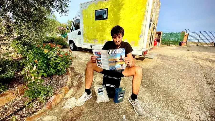 Un viajero sentado con un mapa junto a una furgoneta camper amarilla en un camino de tierra