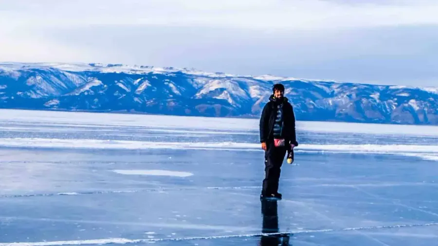 Persona caminando sobre el hielo del lago Baikal con montañas nevadas al fondo