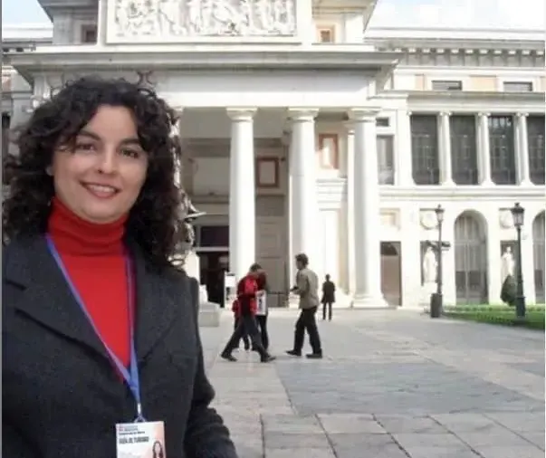 Mujer con credencial frente a un edificio neoclásico