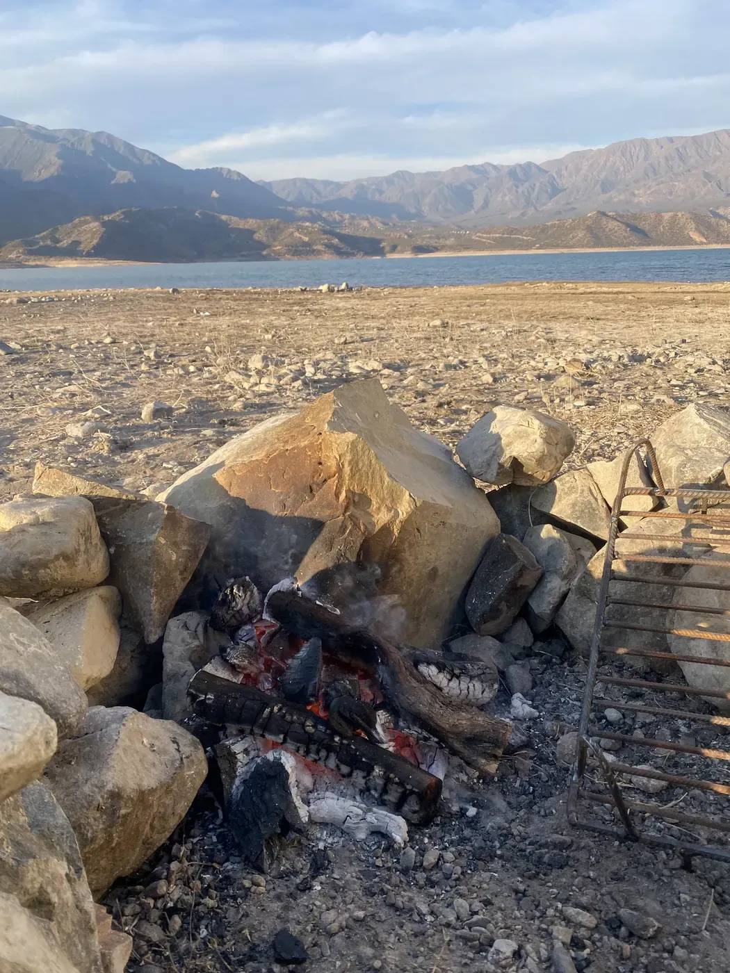 Fuego para el asado entre piedras junto al embalse de Potrerillos, con las montañas al fondo