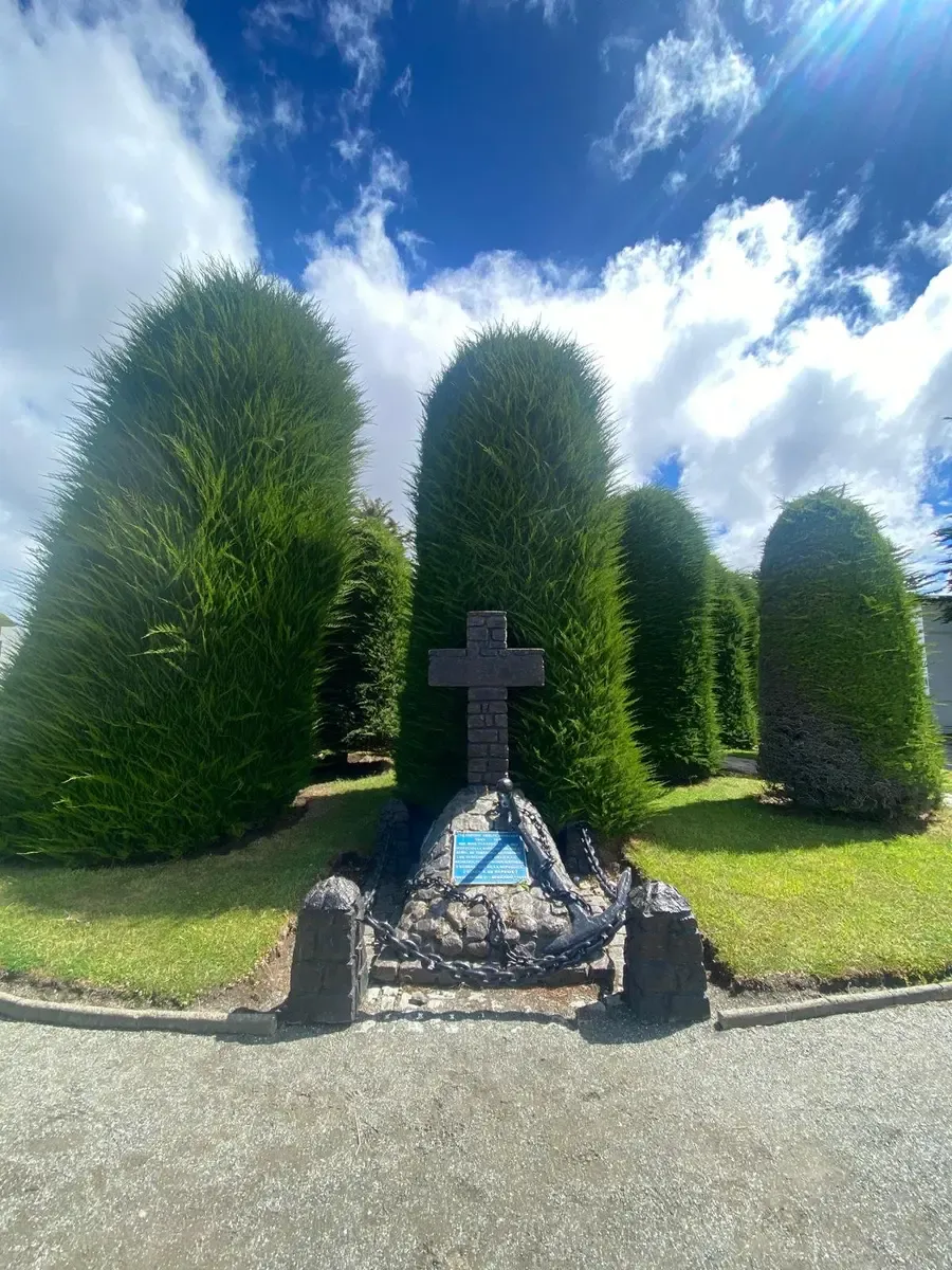 tumba con cruz y detras jardin y arboles