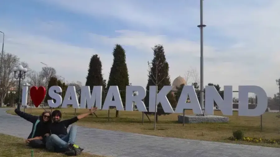 Dos viajeros posando junto al letrero «I love Samarkand» en un parque