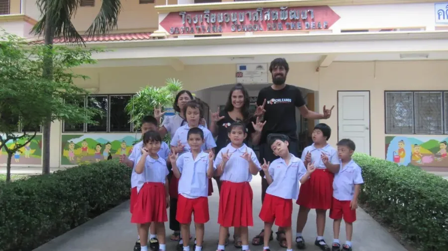Niños con uniforme frente a la escuela de sordos de Pattaya junto a varios adultos