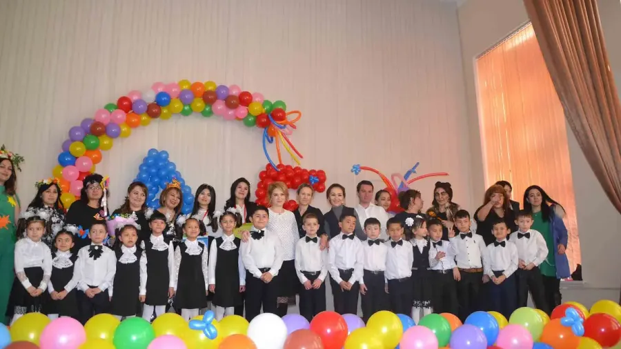Grupo de niños con uniforme bajo un arco de globos de colores en un escenario