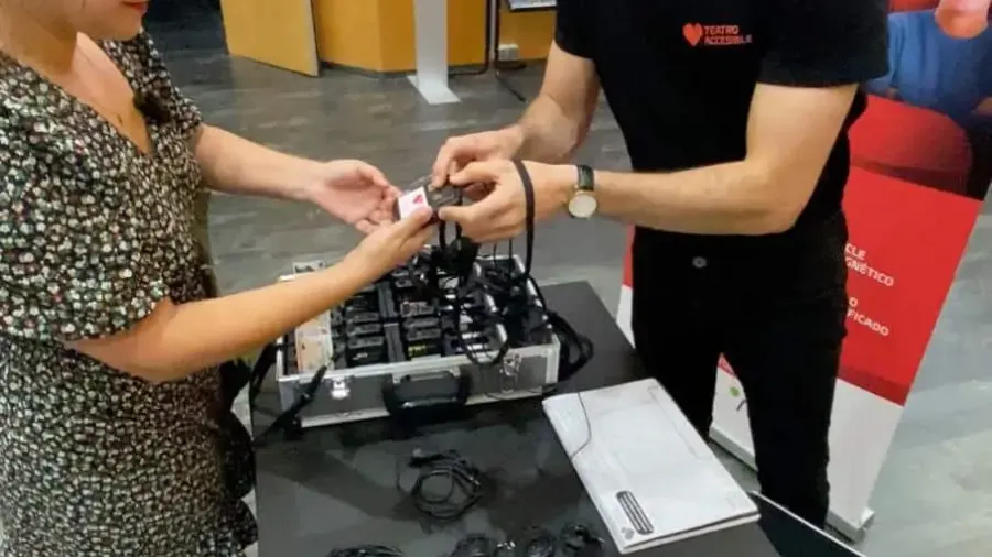 Una persona recibe unos auriculares de un técnico en un mostrador de accesibilidad